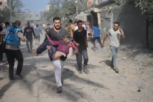 A Palestinian carries a boy wounded during the Israeli bombardment of the Gaza Strip in Deir al-Balah on Sunday. [Hatem Moussa/AP Photo]